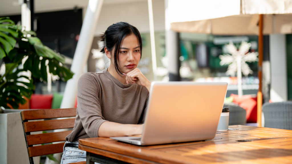 A woman looking at a laptop screen and thinking about how to start a POD business.