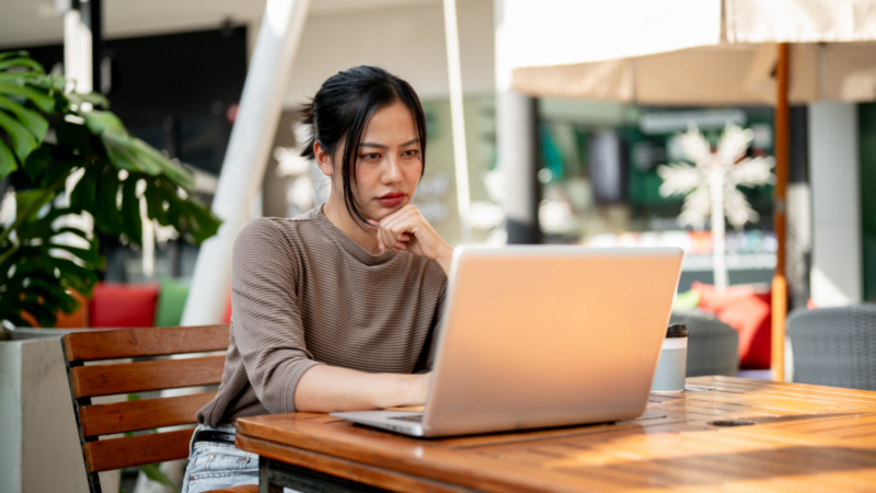 A woman looking at a laptop screen and thinking about how to start a POD business.