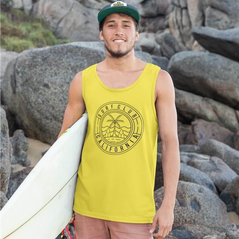 A man holding a surfboard and wearing a yellow tank top with a “Surfclub California” logo.