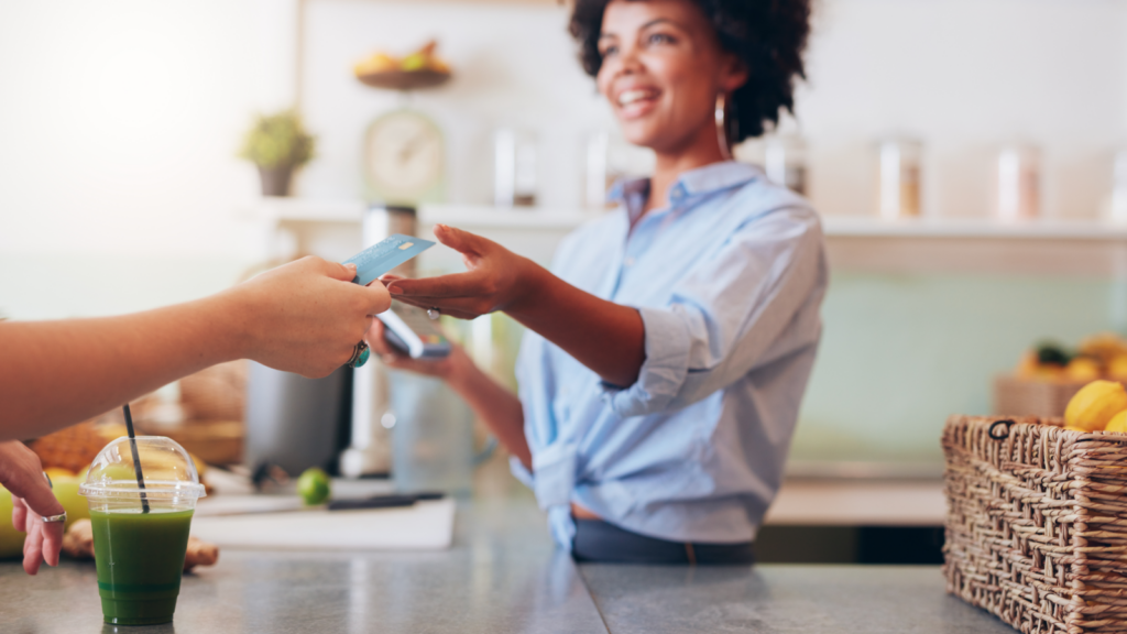 A woman hands a credit card to another person in a transaction setting.