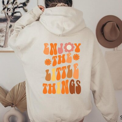 A hoodie design with a playful font and flowers that says "Enjoy the little things."