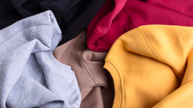 A collection of colorful Gildan sweatshirts in black, gray, beige, red, and yellow, casually laid out.