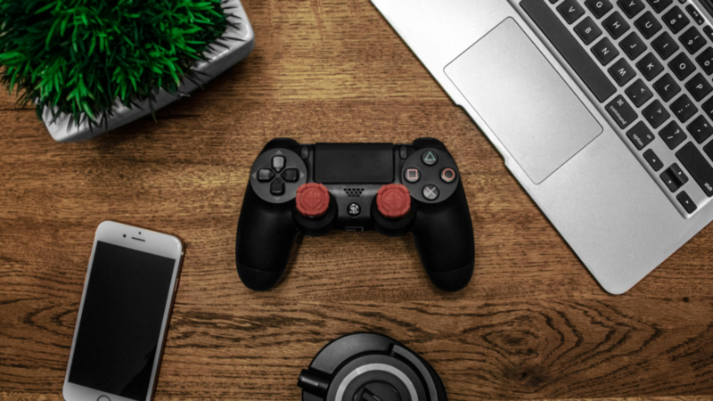 A gamepad, laptop, headphones, green plant, and mobile phone on a wooden surface.