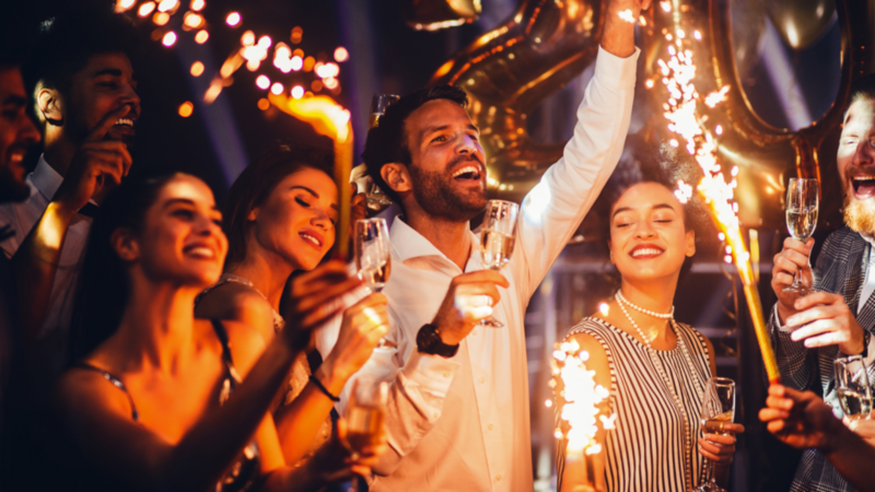 A joyful group of people celebrates with sparklers and champagne at a festive party.