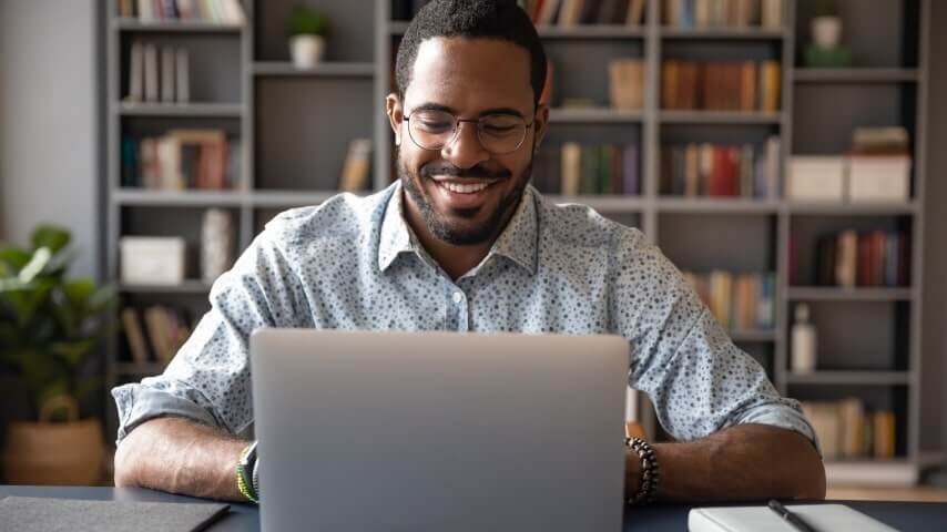 A man with glasses working on his laptop and smiling.