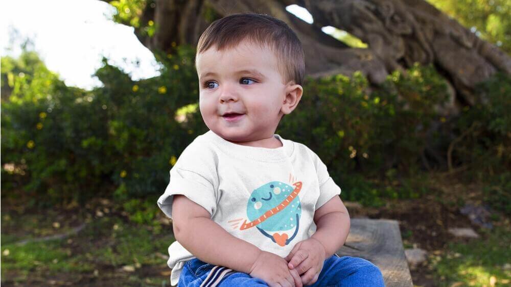 A child wearing a custom white Rabbit Skins 3322 infant t-shirt, with an illustration of planet printed on the front.