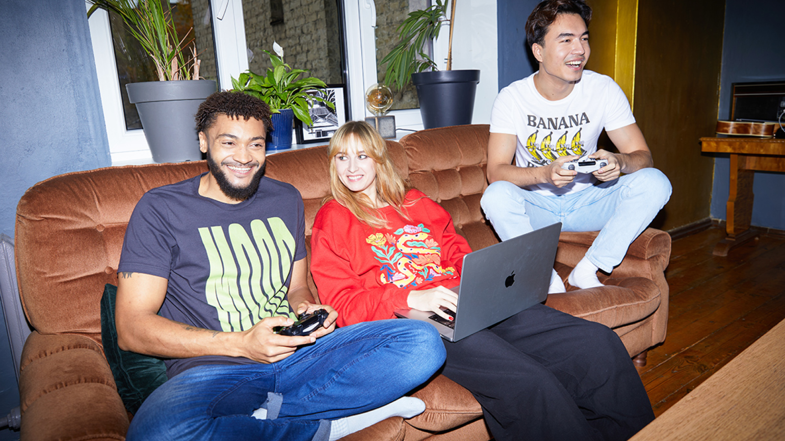 A group of people sitting on a couch in custom t-shirts and hoodies, playing video games.