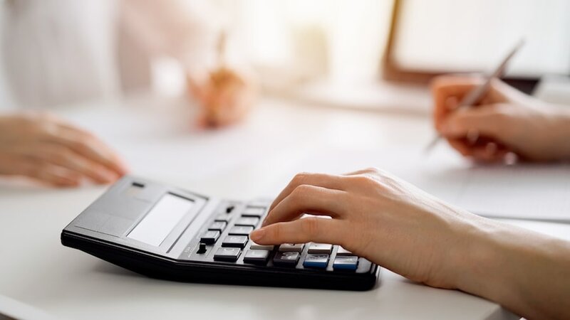 A calculator on a table with a woman’s hand on top of it.