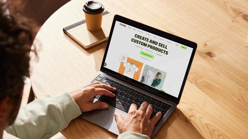A person using a laptop with Printify’s homepage on the screen.