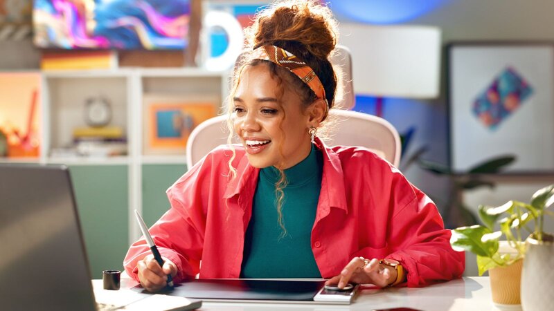 A woman stands before a desk cluttered with boxes and a laptop, engaged in her work environment.