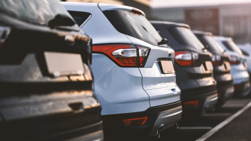 A row of parked cars in a parking lot, showcasing various colors and models under clear blue skies.
