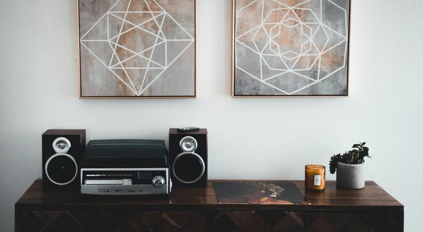 Two posters hang above a counter with a record player, a vinyl record, a candle, and a flower on top.