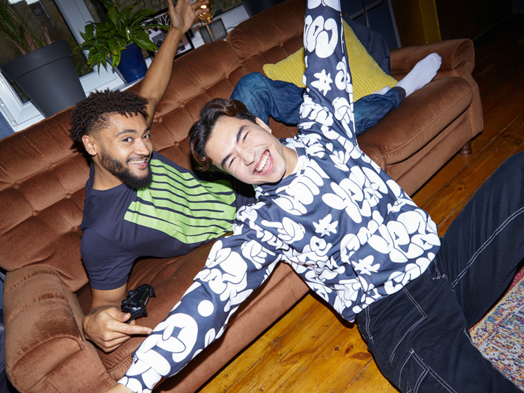 Two men wearing a custom hoodie and t-shirt posing for a picture in front of a couch.