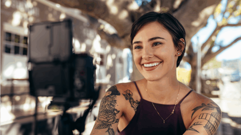 A smiling woman with tattoos poses for the camera, showcasing her joyful expression.