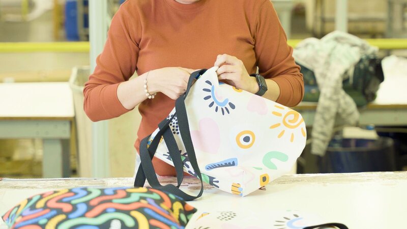 A person is working on a colorful bag in a workshop setting.