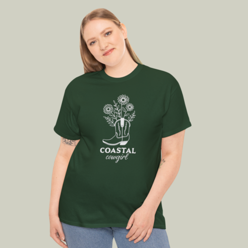 A woman wearing a custom green and gray “Coastal cowgirl” t-shirt on a light olive green background.