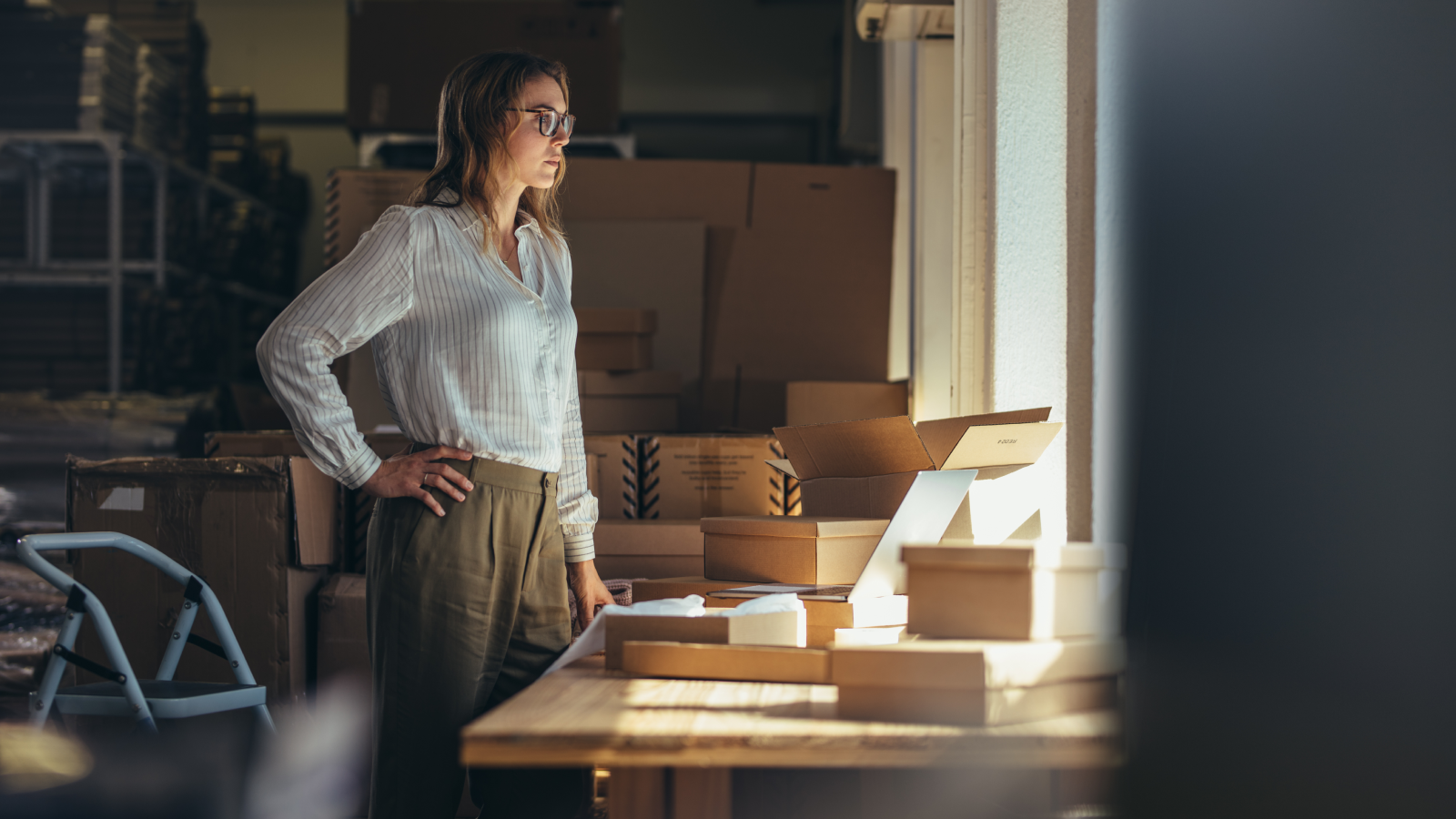 A woman in a white blouse standing in front of a table filled with delivery boxes.