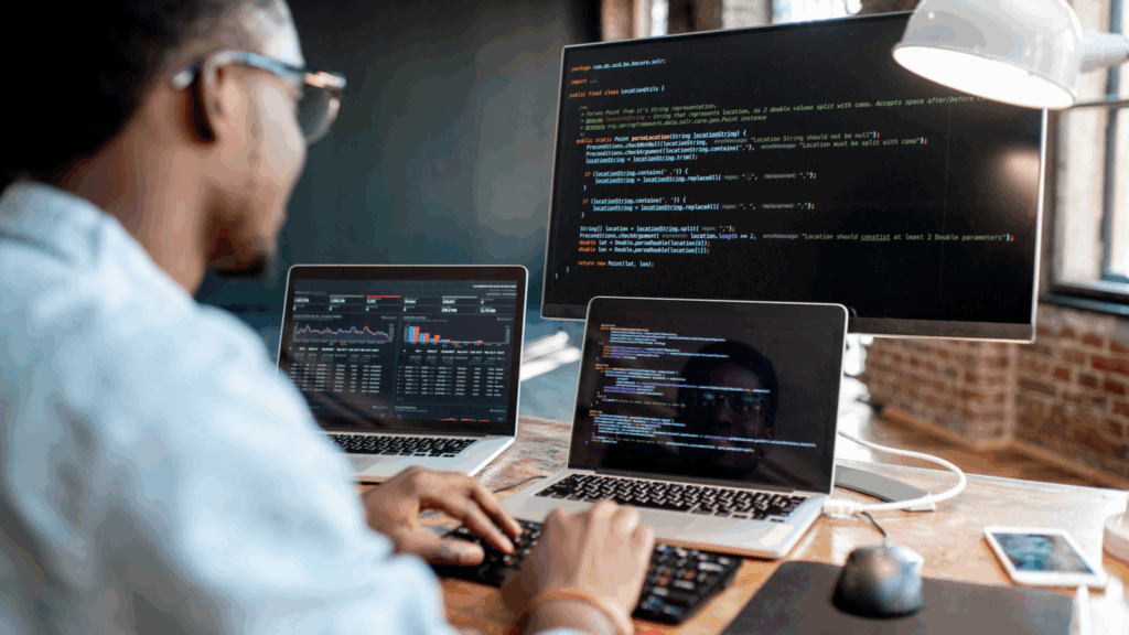 A man coding using two laptops, with one laptop connected to the monitor.