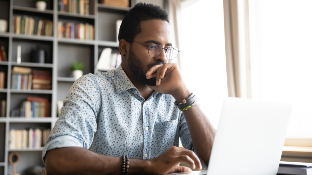 A man with glasses sits at a desk, focused on his laptop.