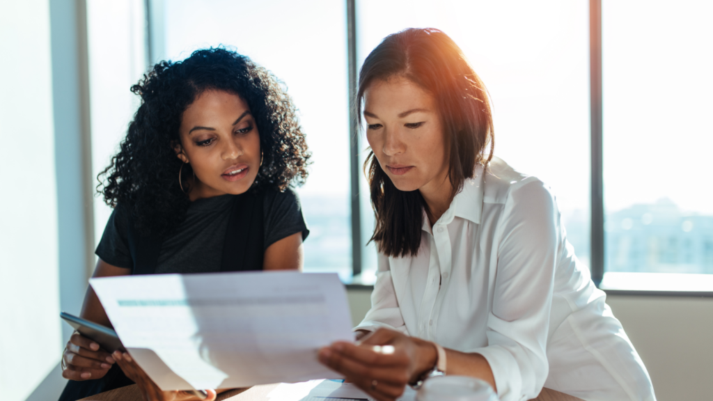 Two women reviewing documents together in a modern office setting.