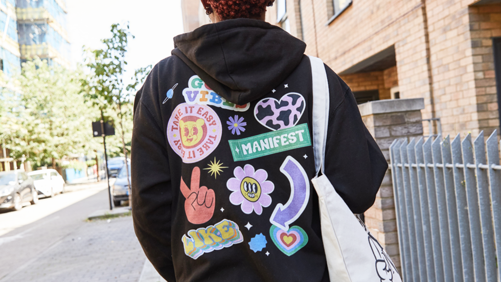 A person wearing a custom black hoodie with a back print consisting of multiple illustrated sticker-like prints.