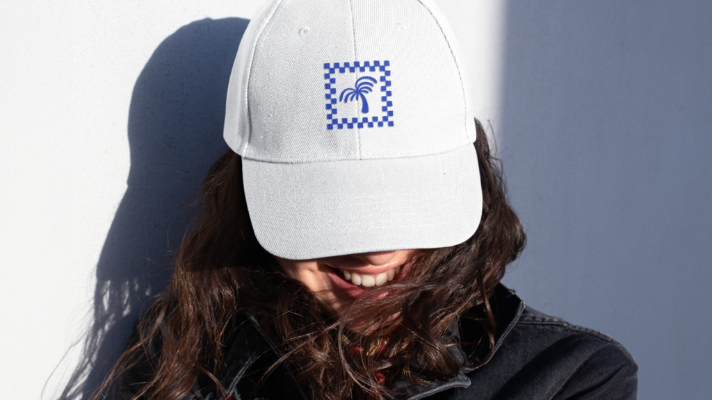 A woman wearing a custom white cap with a blue palm tree logo.