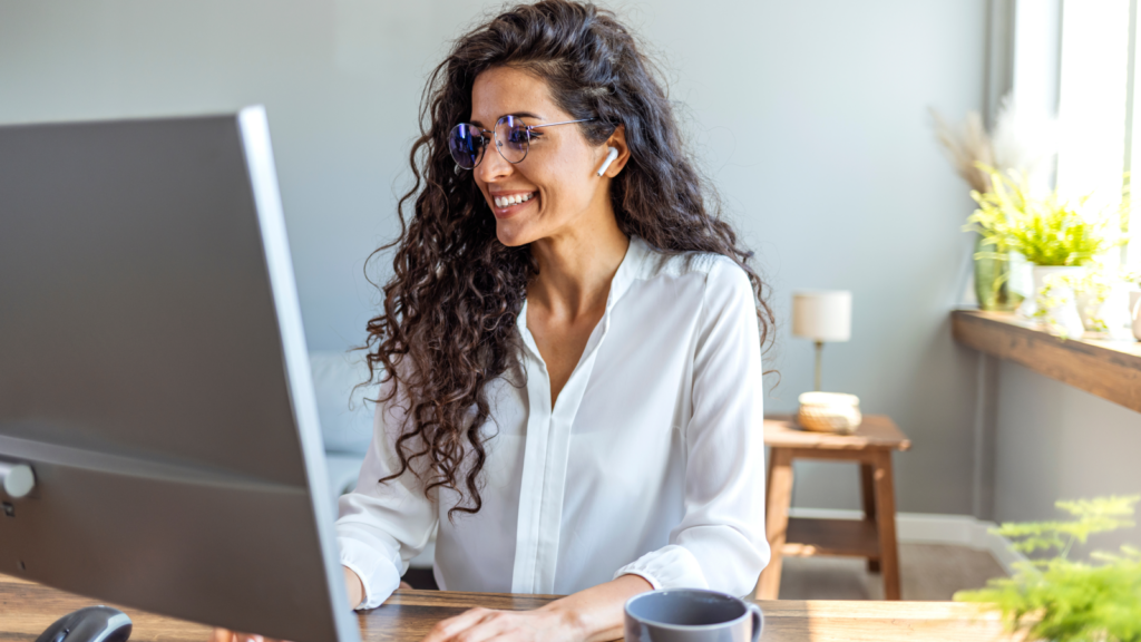 A smiling woman with curly hair is seated at a desk, exuding a cheerful demeanor.