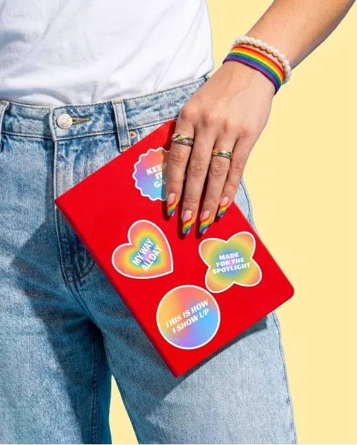A person holds a red notebook adorned with various colorful stickers.