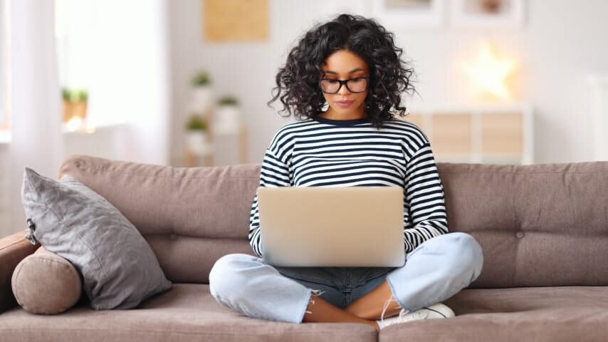 A woman sitting on a couch and working on a laptop.