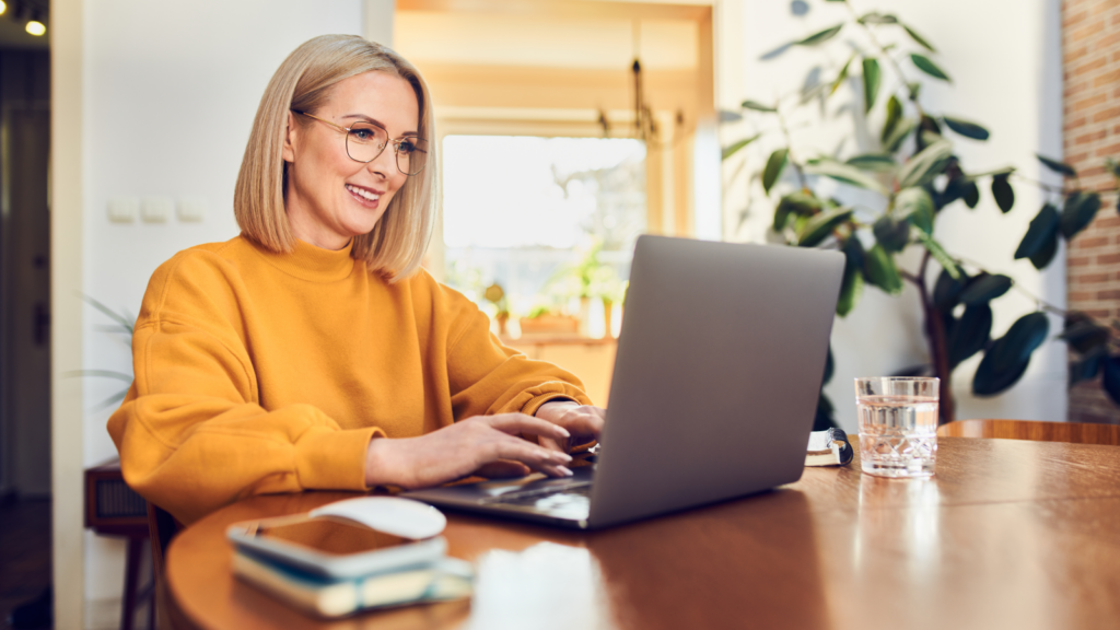A woman wearing glasses is focused on her laptop, engaged in work at a desk.