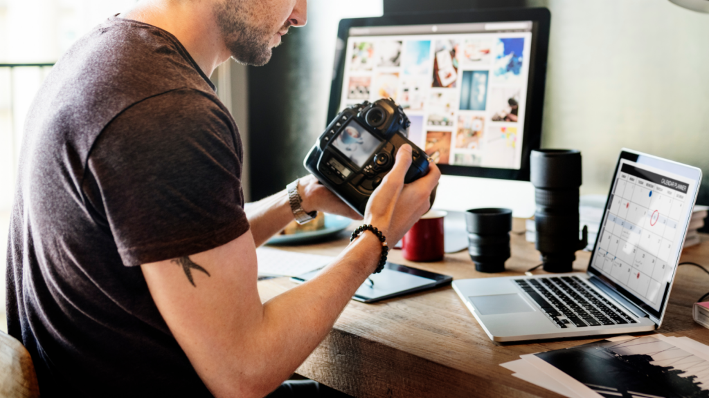 A man is seated at a desk, working on a laptop, with a camera placed next to him.
