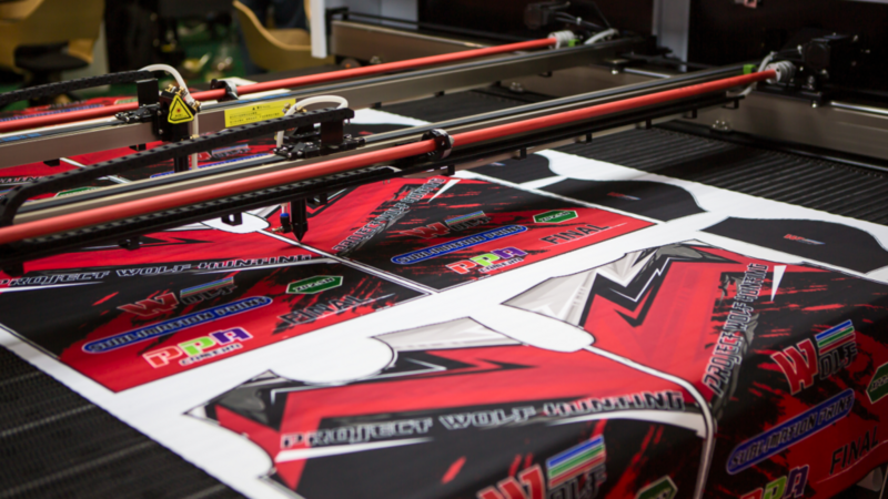 A sublimation printer producing vibrant red and black graphics with logos and text.