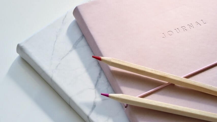 Two blue and pink pastel notebooks with two pencils placed on them.
