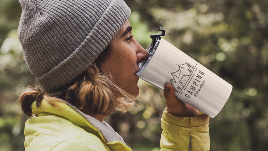 A woman drinking from a custom travel mug in the wilderness.