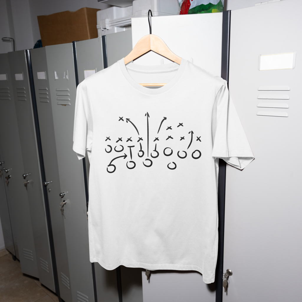 A white t-shirt with a black football play diagram, featuring X’s and O’s with arrows, hangs on a wooden hanger in front of gray lockers.