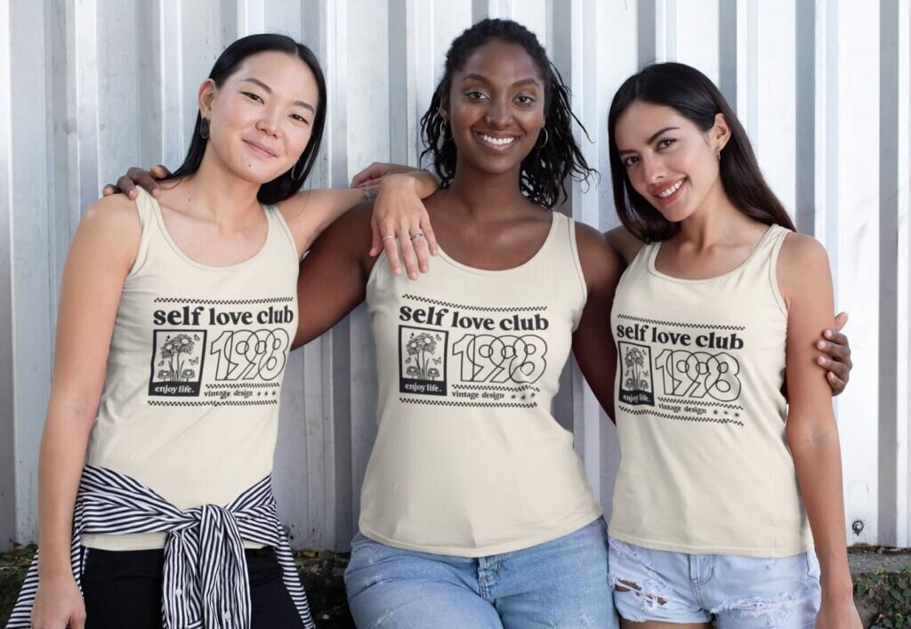 Three women wearing beige custom “Self-love Club 1998” tank tops.