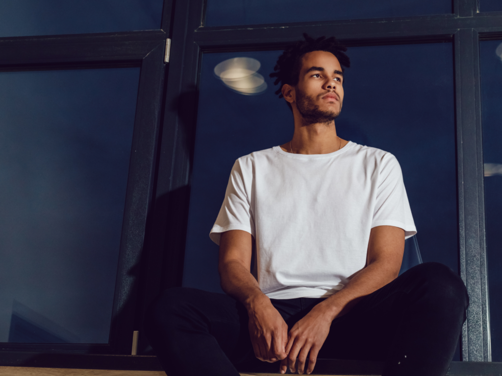 A man in a white t-shirt sits on a window ledge, showcasing a casual and relaxed style for a t-shirt brand.