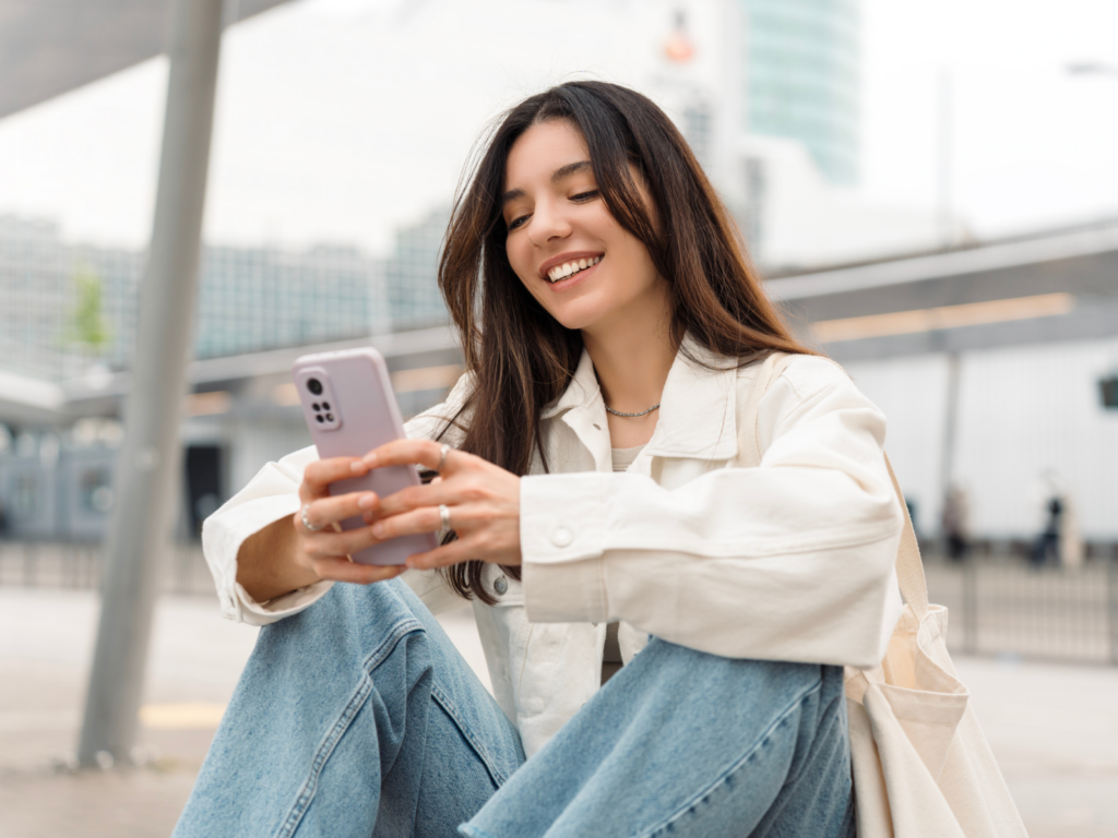 A woman sits on the ground, happily scrolling through Instagram reels on her phone.