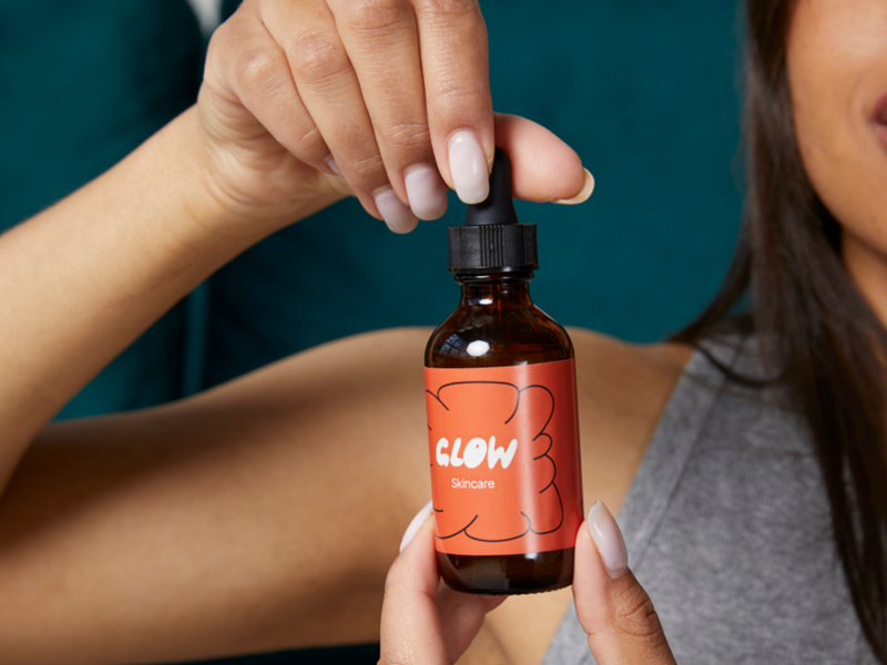 A woman displays a bottle of custom skincare, emphasizing its luminous quality in a serene setting.