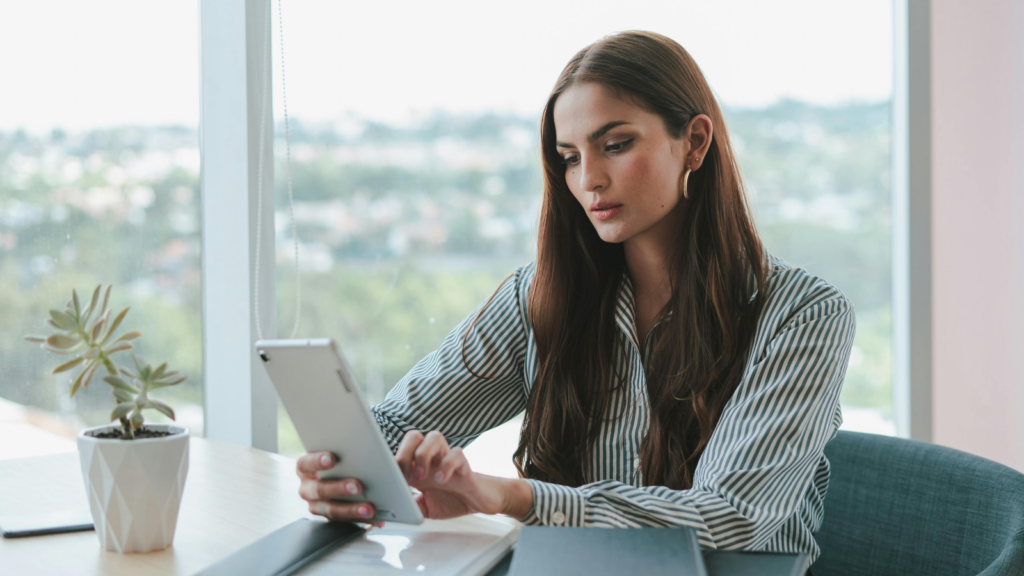 A woman sitting in front of a large window and using a tablet.