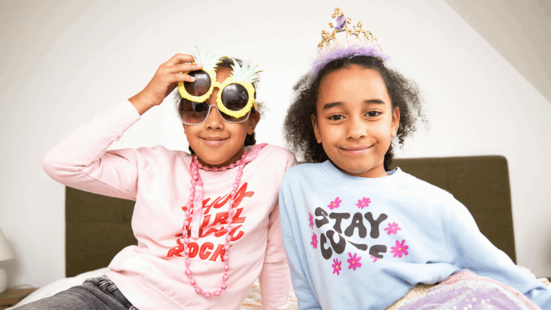 Two young smiling girls wearing different kids' party accessories.