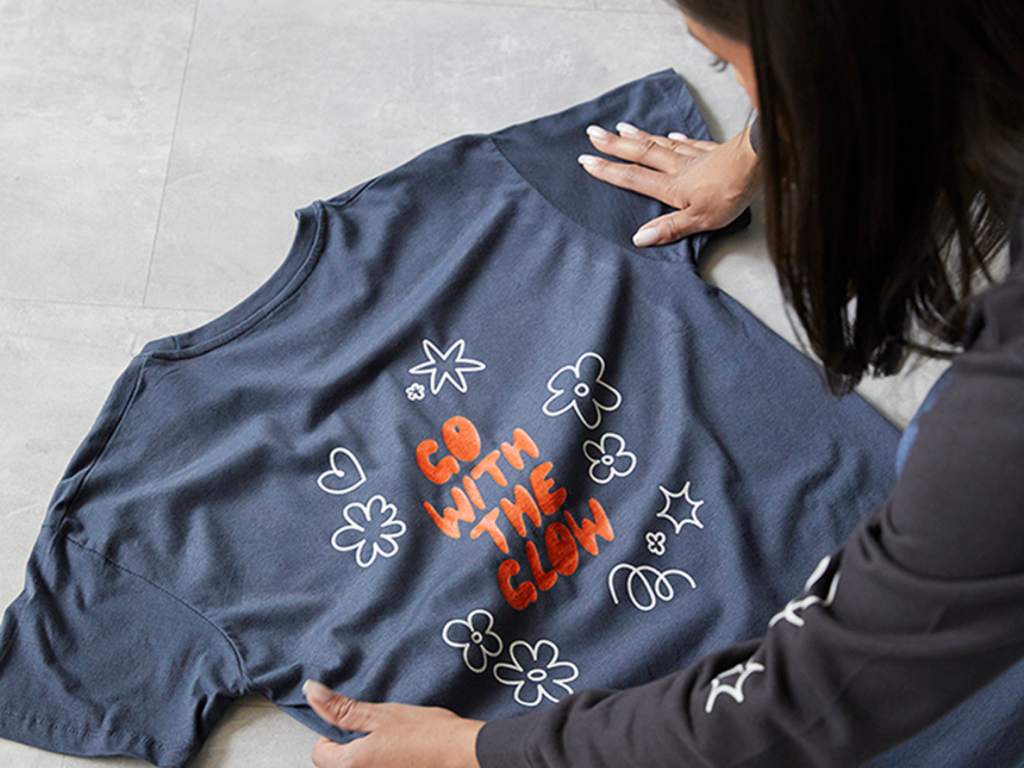 A woman is placing a t-shirt on the floor, looking and print quality.