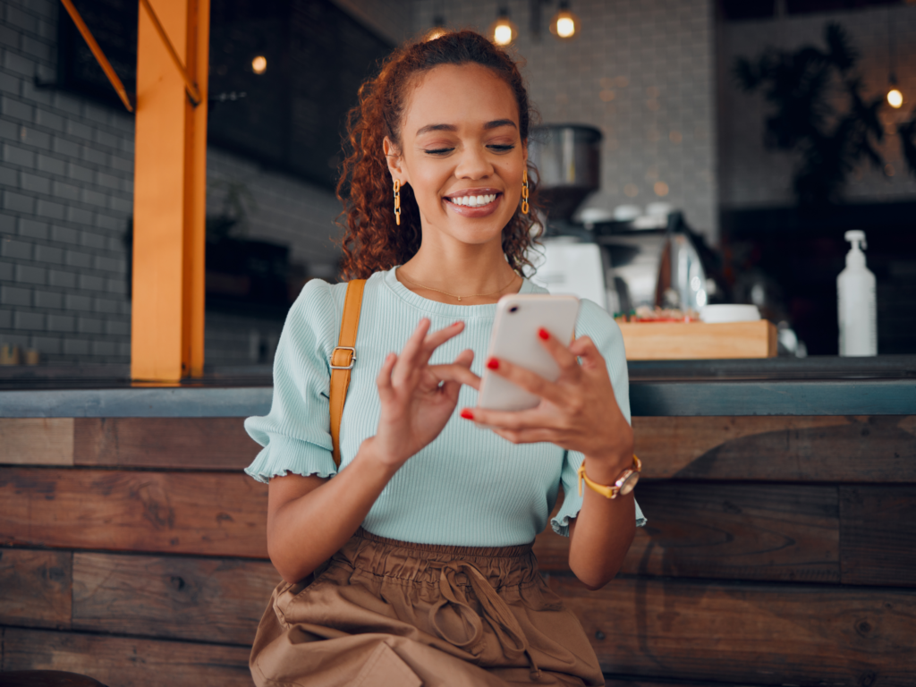 A woman smiling while sitting, holding her phone in a cozy setting.