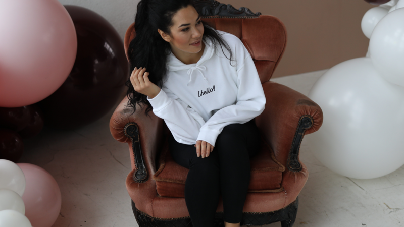 A woman sitting on a vintage armchair, wearing a white hoodie and black leggings, surrounded by balloons.