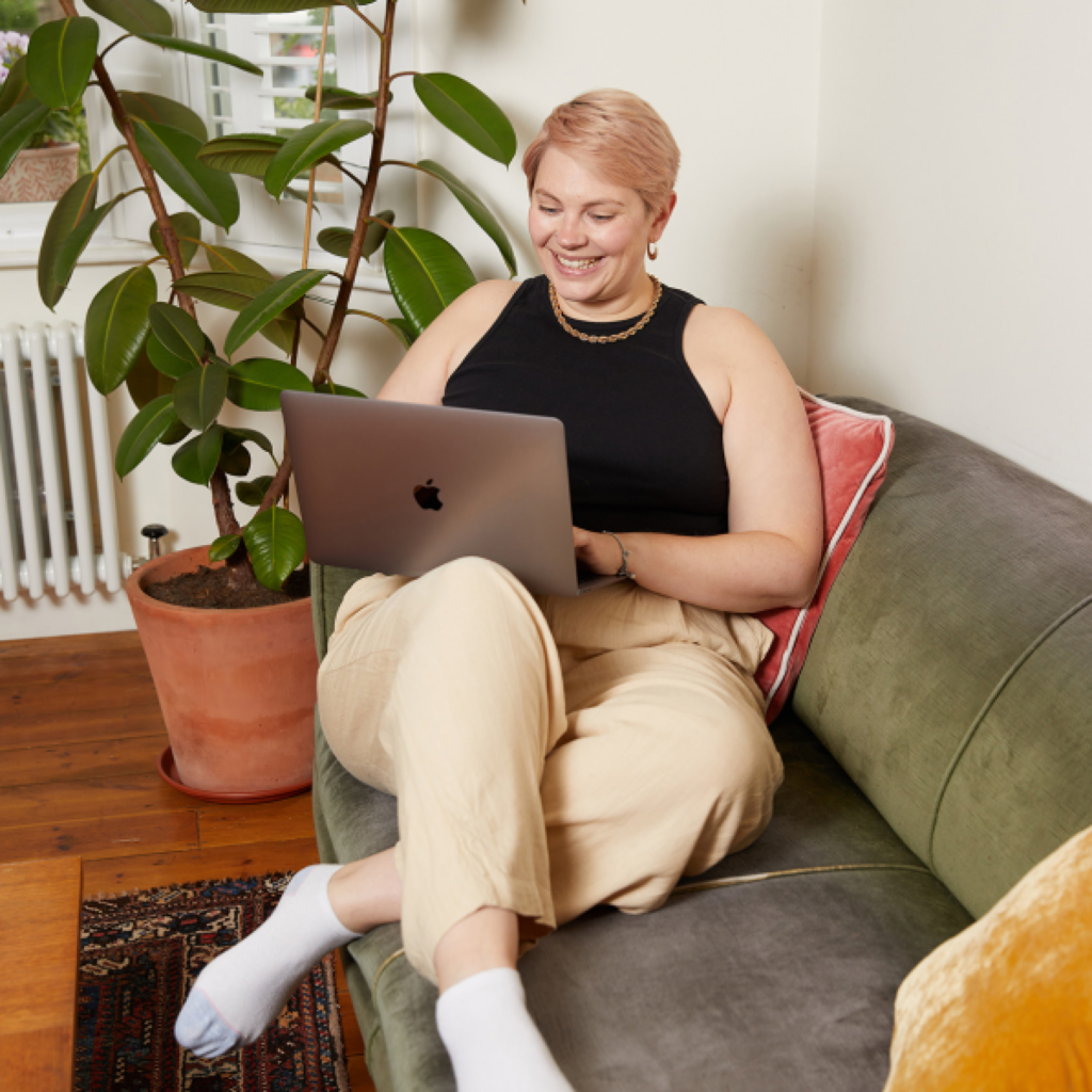 A woman seated on a couch, focused on her laptop, creating a cozy and productive home environment for a side hustle.