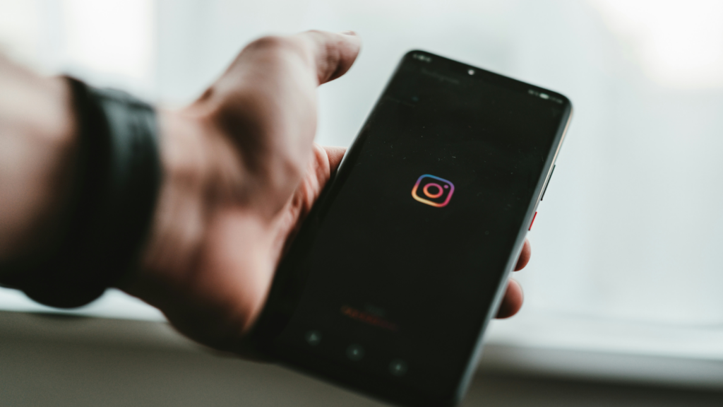 A person holding a mobile phone in one hand while the Instagram app is loading on the screen.
