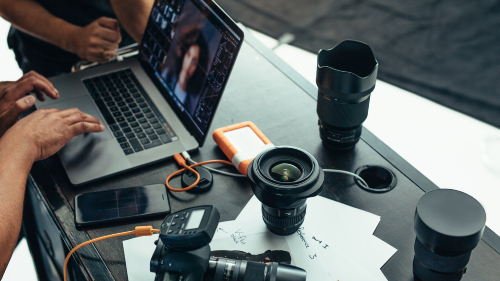 A person editing images using a laptop with a DSLR camera and multiple lenses on the side.