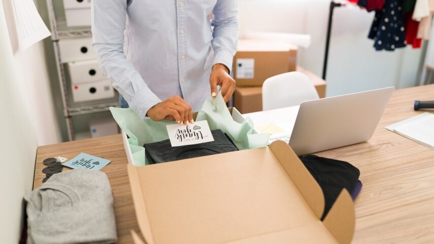 A merchant adding a packaging insert saying “Thank You” to her Etsy order box.