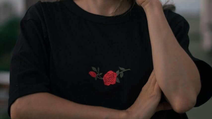 A woman wearing a black t-shirt with an embroidered rose in the middle.