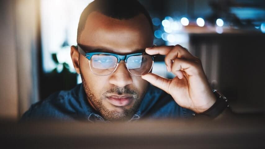 A man adjusting his glasses while looking at a computer screen.